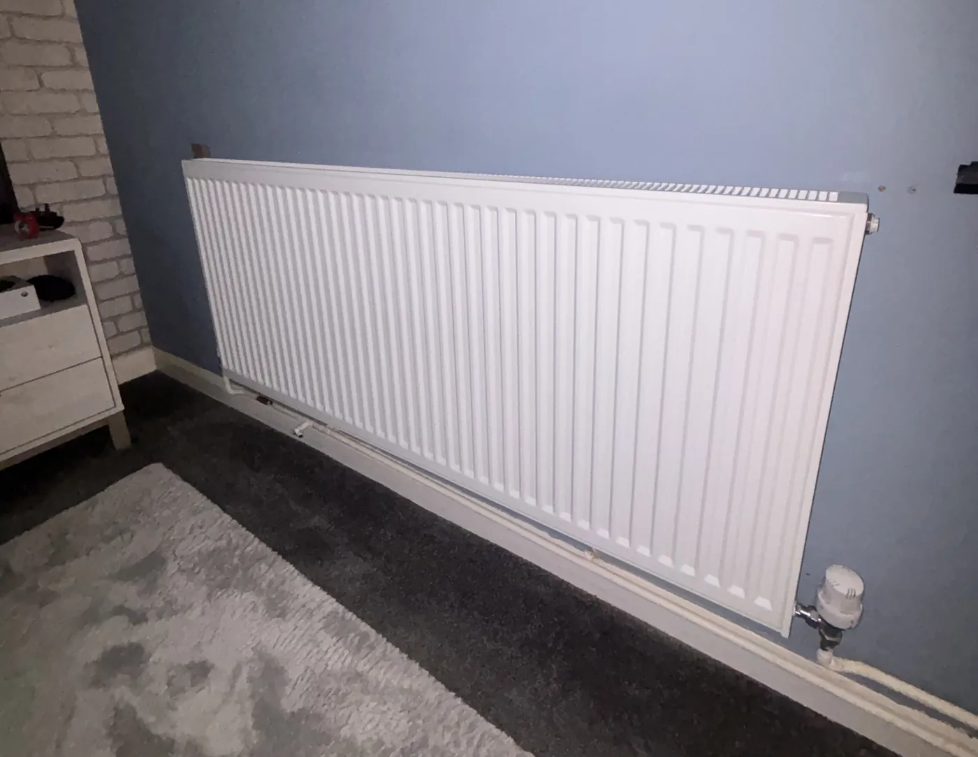 A newly fitted white panel radiator with a thermostatic valve in a bedroom