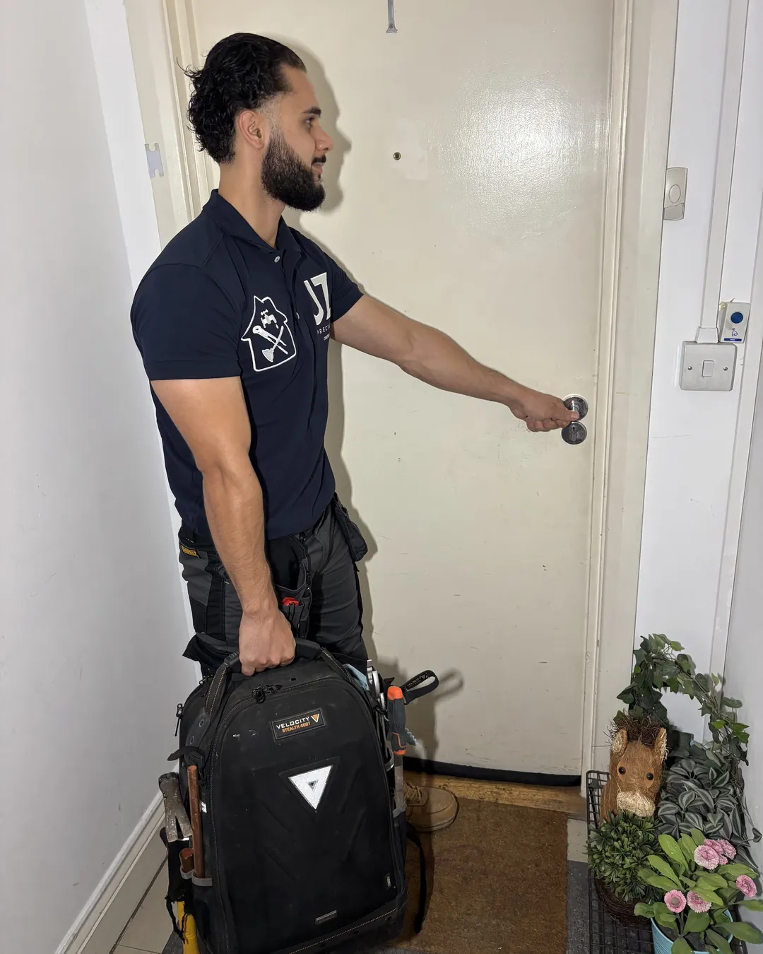 A JZ Precision plumber in branded workwear arriving at a customer's front door with his tool bag