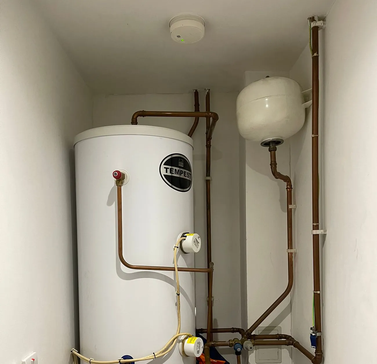 An unvented hot water cylinder with neat copper pipework in a cupboard